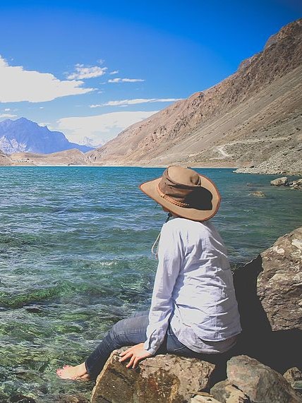 A person sitting by Sadpara Lake with mountains in the background